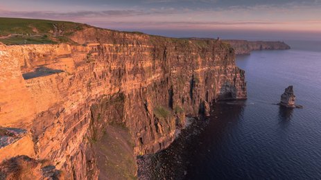 Die beeindruckenden Cliffs of Moher erheben sich majestätisch über den ruhigen Atlantik, beleuchtet von warmem Abendlicht.