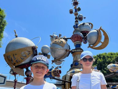 Zwei Kinder stehen vor einem bunten, futuristischen Karussell in Disneyland, umgeben von strahlend blauem Himmel.
