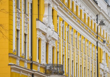 Die Fassade eines prächtigen gelben Gebäudes mit kunstvollen weißen Verzierungen und einem eleganten Balkon.
