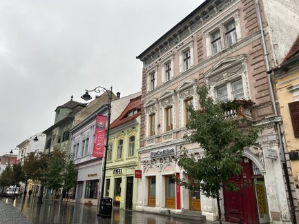 Bunte historische Gebäude säumen die Straße in Sibiu, während der Regen die glänzenden Pflastersteine reflektiert.