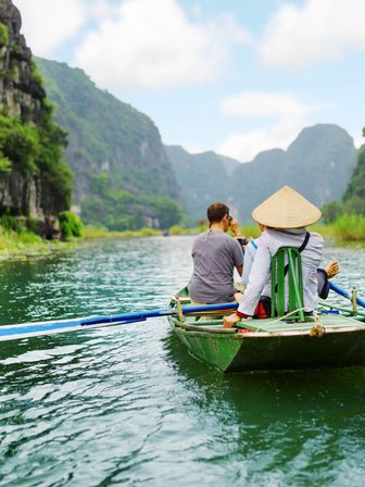 Zwei Personen sitzen in einem Boot und genießen die ruhige Landschaft mit hohen, bewaldeten Klippen im Hintergrund.