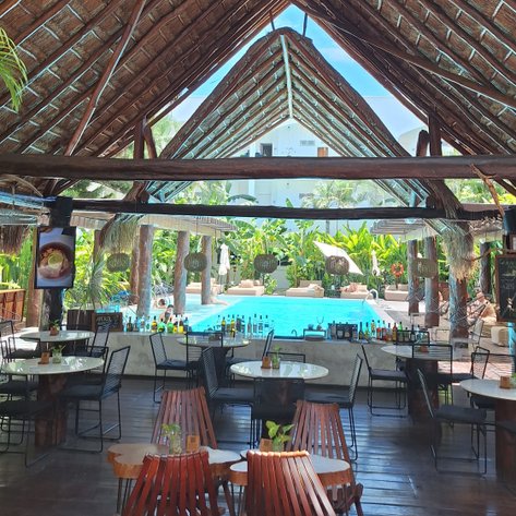 Ein einladender Außenbereich mit einem Strohdach, umgeben von Palmen und einem glitzernden Pool im Hintergrund.