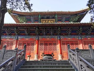 Ein prächtiges, traditionelles chinesisches Kloster mit bunten Dachziegeln und kunstvollen Verzierungen, umgeben von Bäumen.