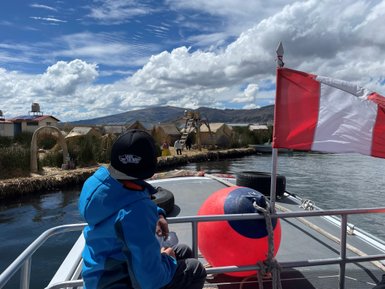 Ein Junge sitzt auf einem Boot und blickt auf die schwimmenden Inseln des Titicaca-Sees unter einem bewölkten Himmel.