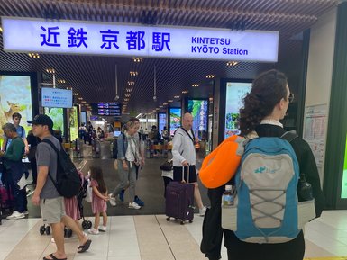 Eine Reisende mit einem blauen Rucksack steht am Kintetsu Kyoto Bahnhof, umgeben von anderen Passagieren und Gepäck.