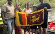 Eine Gruppe von fünf Personen steht am Ufer, während sie stolz die Flagge von Sri Lanka halten, umgeben von üppiger Natur.