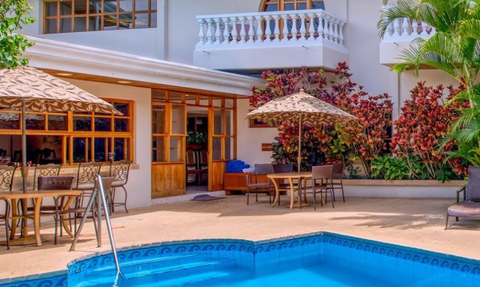 Ein einladender Außenbereich mit einem blauen Pool, umgeben von tropischen Pflanzen und einem gemütlichen Essbereich.