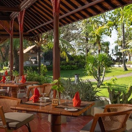 Ein elegantes Restaurant im Freien mit Holztischen, roten Servietten und Blick auf üppige tropische Pflanzen.