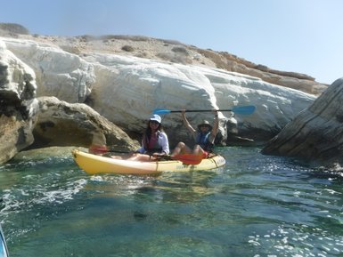 Zwei Personen paddeln fröhlich in einem gelben Kajak zwischen beeindruckenden weißen Felsen und klarem Wasser.