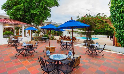 Ein einladender Außenbereich mit blauen Sonnenschirmen und Tischen um einen Pool, umgeben von üppigem Grün.