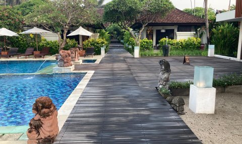 Ein ruhiger Poolbereich mit blauen Fliesen, umgeben von üppigem Grün und kunstvollen Steinfiguren, die eine entspannende Atmosphäre schaffen.