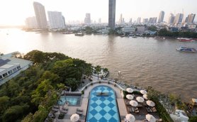 Ein Blick auf den Pool des Chatrium Hotels, umgeben von Palmen und Liegen, mit der Stadt Bangkok im Hintergrund.