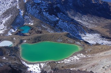 Die beeindruckende Landschaft des Tongariro-Nationalparks zeigt leuchtend grüne Seen, umgeben von schneebedeckten Bergen.