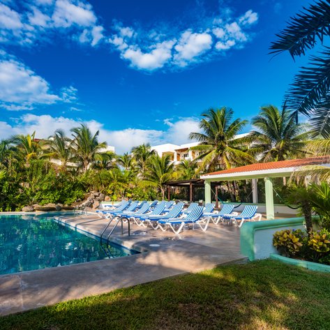 Ein einladender Poolbereich mit blauen Liegen, umgeben von üppigem Grün und Palmen unter einem strahlend blauen Himmel.