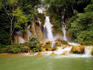 Ein majestätischer Wasserfall stürzt über grüne Felsen, umgeben von üppigem, tropischem Wald und klarem Wasser.