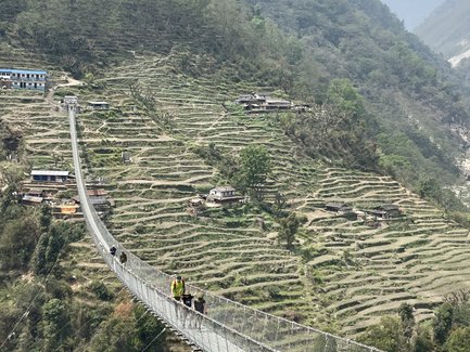 Eine schmale Hängebrücke verbindet zwei Berghänge, während Wanderer über die beeindruckende Landschaft gehen.