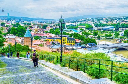 Ein malerischer Blick auf Tiflis mit bunten Gebäuden und einer Seilbahn, die über die Stadt schwebt.