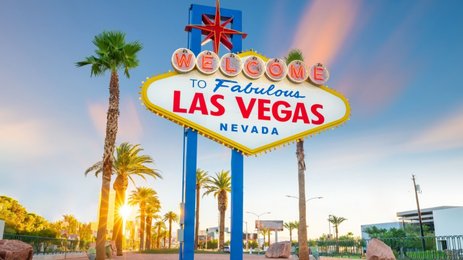 Das berühmte Willkommensschild von Las Vegas strahlt in leuchtenden Farben, umgeben von Palmen und einem klaren Himmel.