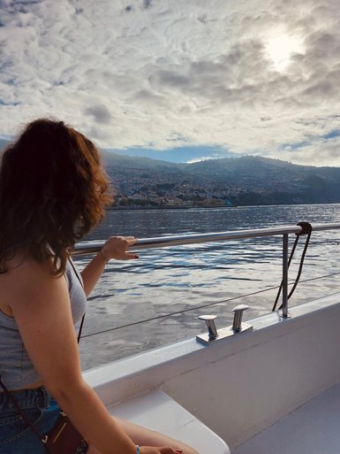Eine Frau mit lockigem Haar sitzt auf einem Boot und blickt auf die malerische Küstenlandschaft Madeiras.