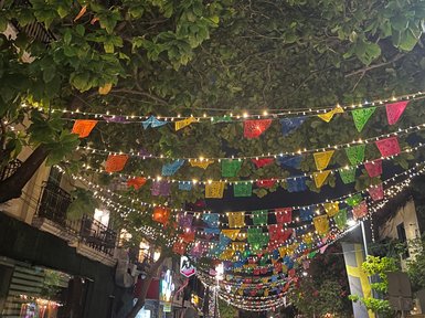 Bunte Papierbanner hängen über einer belebten Straße, umgeben von üppigem Grün und sanftem Licht in der Nacht.