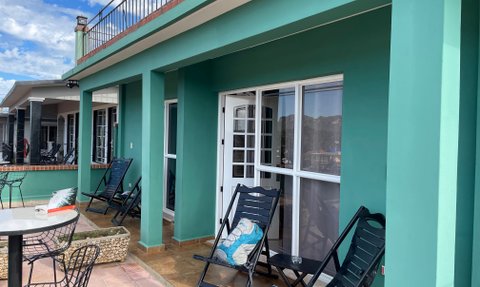 Eine Terrasse mit grünen Wänden, auf der schwarze Liegestühle und ein Tisch stehen, umgeben von einer malerischen Landschaft.