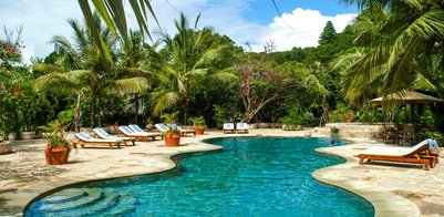 Ein einladender Pool umgeben von üppigen Palmen und bunten Blumen, ideal für entspannende Tage im Freien.