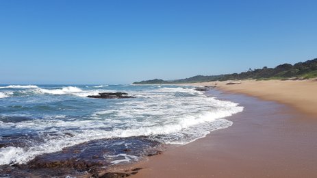 Ein ruhiger Strand mit sanften Wellen, die auf den goldenen Sand treffen, unter einem strahlend blauen Himmel.