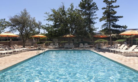 Ein einladender Pool mit klarem Wasser, umgeben von Liegen und Sonnenschirmen, unter einem strahlend blauen Himmel.