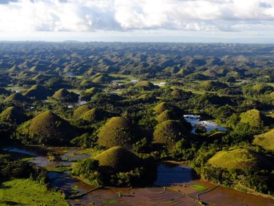 Die sanften, grünen Hügel der Chocolate Hills erstrecken sich über eine weite Landschaft, umgeben von üppiger Vegetation.