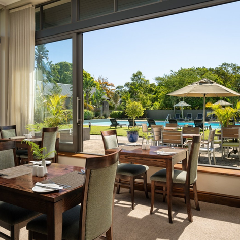 Ein elegantes Restaurant mit Holztischen und Stühlen, das einen Blick auf einen sonnigen Poolbereich bietet.