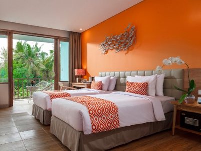 Ein modernes Hotelzimmer mit zwei Betten, orangefarbenen Akzenten und Blick auf üppige Palmen durch große Fenster.