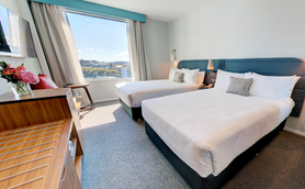 Ein modernes Hotelzimmer mit zwei Einzelbetten, großen Fenstern und einem Blick auf die Stadt Auckland.