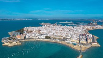 Eine Luftaufnahme von Cádiz zeigt die weiße Stadtarchitektur, die sich entlang der Küste erstreckt, umgeben von klarem, blauem Wasser.