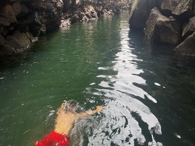 Ein Junge schwimmt entspannt in einem ruhigen, grünen Wasser zwischen hohen, steilen Felsen.