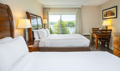Ein helles Hotelzimmer mit zwei Betten, einem Tisch und einem Fenster, das einen Blick auf die Natur bietet.