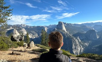 Ein junger Mann sitzt auf einem Felsen und blickt auf die majestätischen Berge des Yosemite Nationalparks.