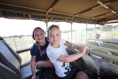 Zwei Mädchen sitzen in einem offenen Safari-Jeep und blicken in die Kamera - Namibia Urlaub mit Kindern