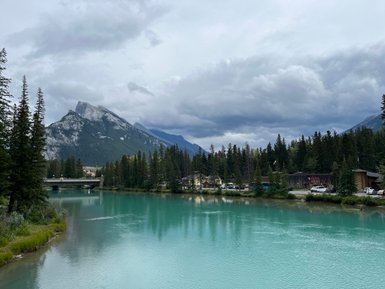 Ein ruhiger Fluss mit türkisfarbenem Wasser fließt durch eine bewaldete Landschaft, umgeben von majestätischen Bergen.