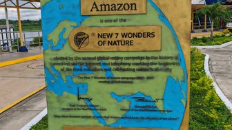Ein Schild, das den Amazonas als eines der neuen sieben Naturwunder der Welt auszeichnet, umgeben von grüner Landschaft.