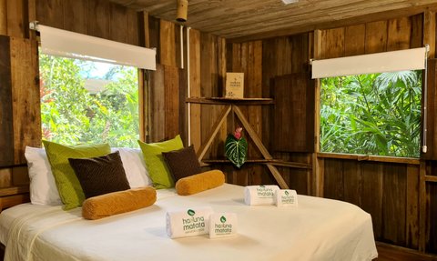 Ein gemütliches Zimmer im Amazonas mit einem großen Bett, bunten Kissen und Blick auf die grüne Natur durch große Fenster.