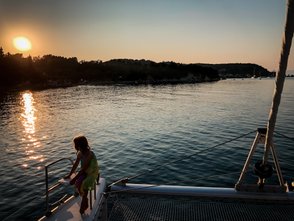 Ein Mädchen sitzt auf einem Boot und beobachtet den Sonnenuntergang über dem ruhigen Wasser von Notos Beach auf Korfu.
