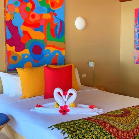 Ein helles Hotelzimmer mit bunten Wandgemälden, einem großen Bett und dekorativen Handtüchern in Form von Schwänen.