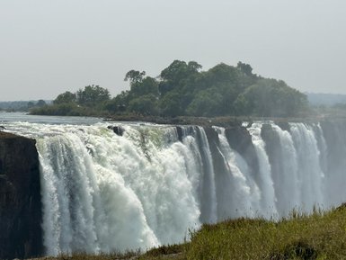 Die majestätischen Victoriafälle stürzen mit kraftvollem Wasser in die Tiefe, umgeben von üppigem Grün und Nebel.