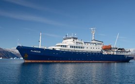 Das Forschungsschiff Plancius liegt ruhig im Wasser, umgeben von majestätischen Bergen und Eisbergen im Hintergrund.