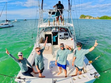 Eine Gruppe von vier Anglern steht auf dem Deck eines Bootes im Nordpazifik, alle jubeln und zeigen mit einem Finger nach oben.