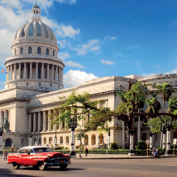 Das beeindruckende Kapitol in Havanna, umgeben von historischen Autos und üppigem Grün, strahlt koloniale Eleganz aus.