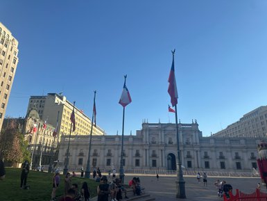 Im Herzen von Santiago stehen mehrere Flaggen vor einem historischen Gebäude, während Menschen im Park entspannen.