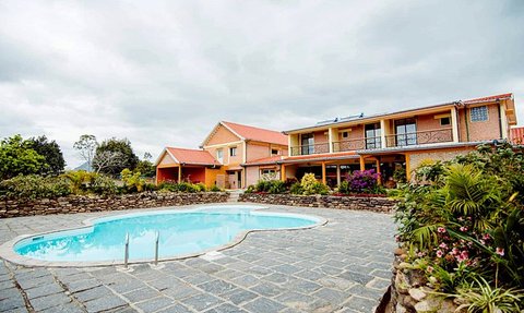 Ein einladender Pool umgeben von bunten Blumen und einem charmanten Hotel im Hintergrund unter einem bewölkten Himmel.