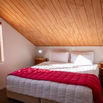 Ein gemütliches Schlafzimmer mit einem großen Bett, das mit einer roten Decke und weißen Kissen dekoriert ist.