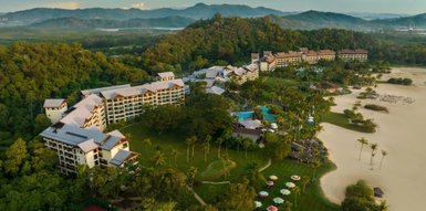 Ein luxuriöses Resort eingebettet in üppige Natur, mit mehreren langen Gebäuden und einem glitzernden Poolbereich.